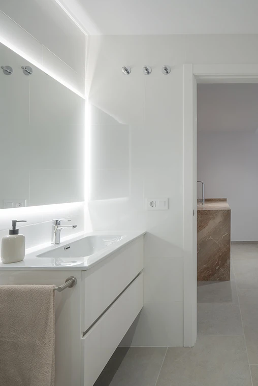 Baño de diseño minimalista en blanco con espejo retroiluminado, parte de un proyecto de construcción de lujo en Castellón realizado por nuestra empresa constructora