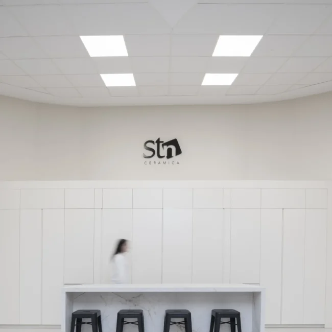 Diseño de corporate moderno en STN Cerámica con barra de mármol blanco, taburetes industriales negros y claraboya cenital que aporta iluminación natural al espacio al comedor