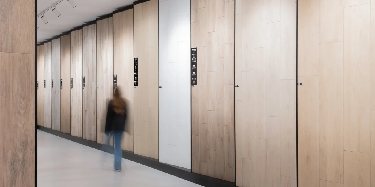 Amplio pasillo de showroom cerámico con paneles expositores de gres efecto madera, iluminación técnica de carril y diseño de circulación diáfana.