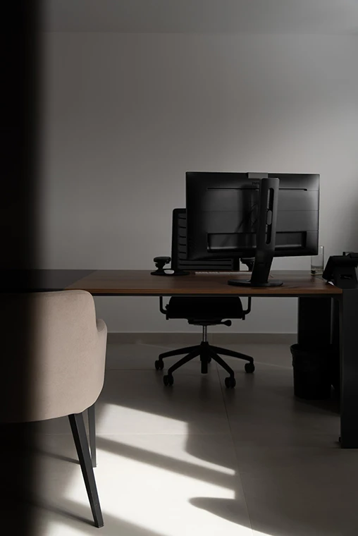 Puesto de trabajo con escritorio de madera natural, silla de oficina ergonómica y detalles de iluminación natural sobre pavimento porcelánico.
