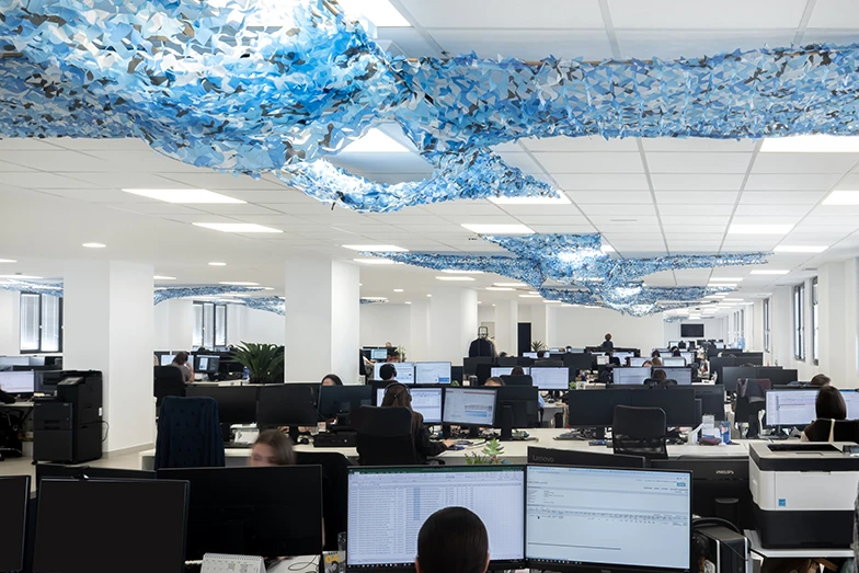 Oficinas de planta abierta de STN Cerámica con puestos de trabajo operativos y original decoración de techo con redes técnicas azules para mejorar la acústica y el diseño.