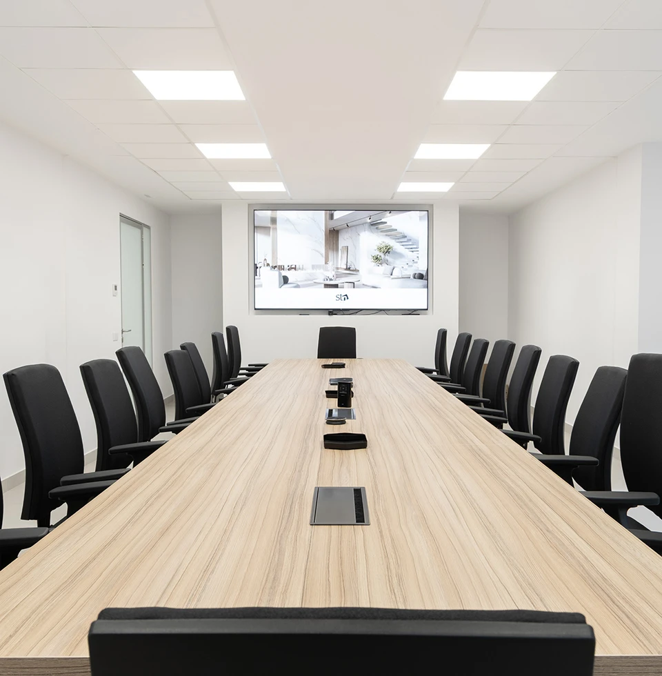 Sala de reuniones moderna de STN Cerámica con gran mesa de madera, sillas ergonómicas negras y pantalla de alta definición para presentaciones corporativas.
