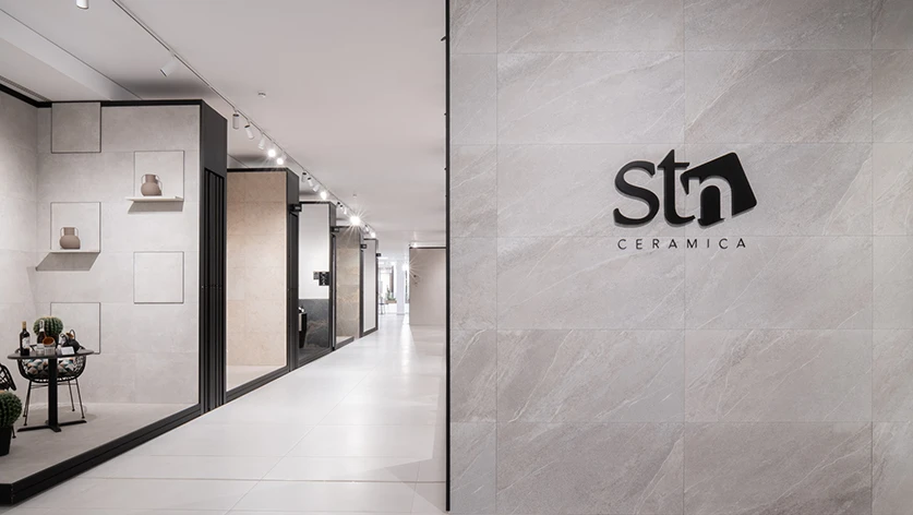 Exposición de pavimentos y revestimientos cerámicos en el showroom de STN Cerámica, con logotipado sobre pared de gres porcelánico de gran formato.
