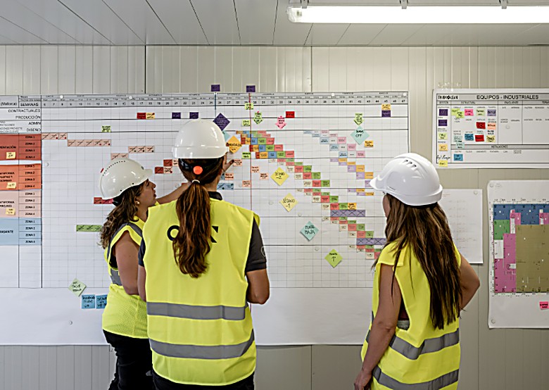 Equipo de OCN Grupo con casco y chaleco de seguridad revisando la planificación de obra en el tablero de producción
