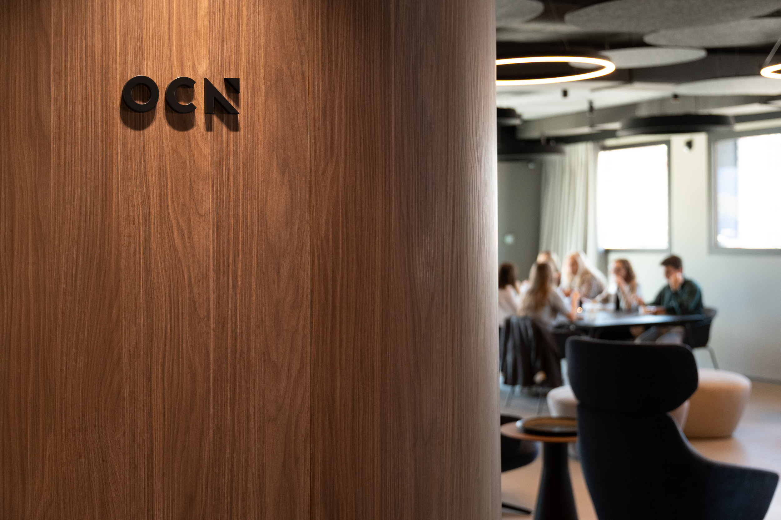 Zona común con mesa de porcelánico, zona lounge y pantalla con el logo de OCN en las oficinas centrales de Castellón